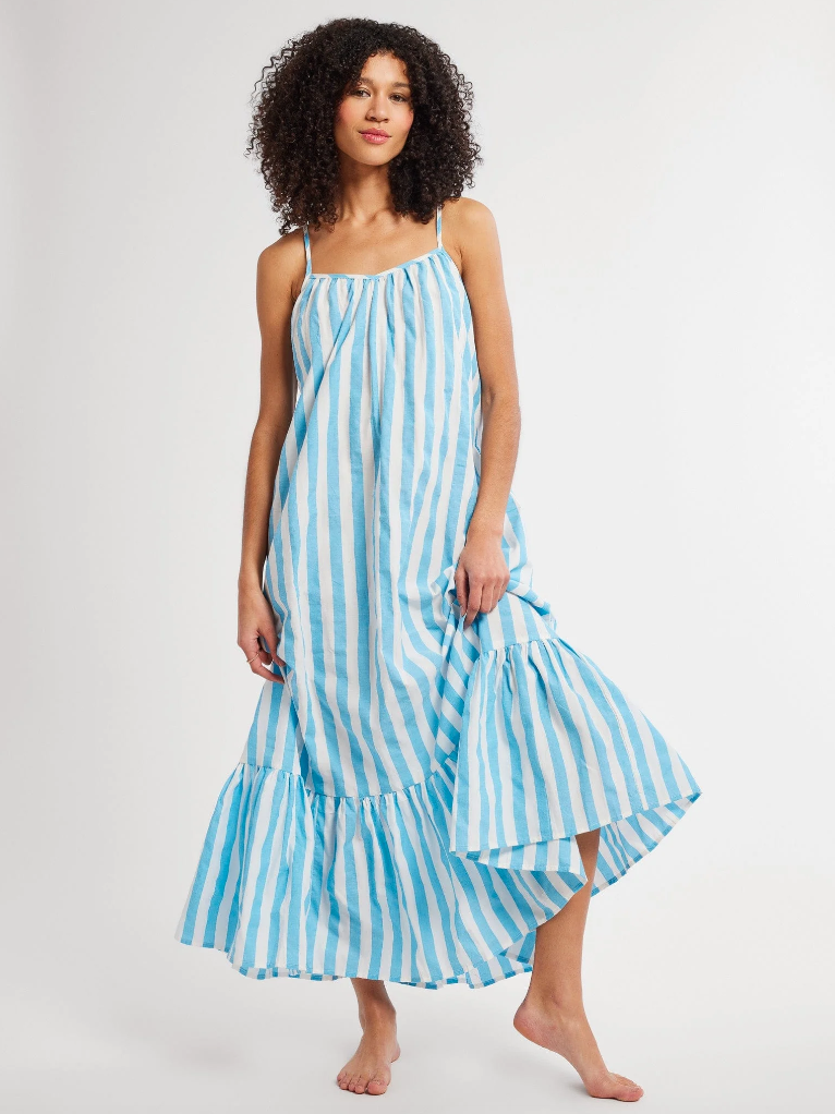 A woman with curly hair, wearing a blue and white striped, sleeveless Sienna Dress with a ruffled hem, stands barefoot on a white background in Scottsdale, Arizona.