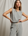 A woman poses confidently in the ELLIE terry banded tank by Perfectwhitetee, styled with matching gray sweatpants with white drawstrings, standing against a draped light fabric background.