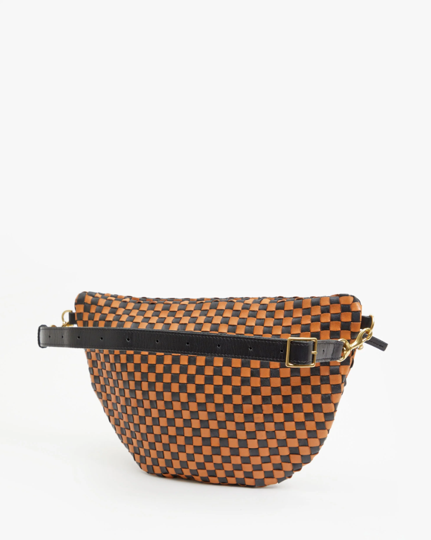An orange and brown checkered crossbody bag with a black adjustable strap and metallic buckle, displayed against a white background in Arizona style, the Grande Fanny Woven Checker by Clare Vivier.