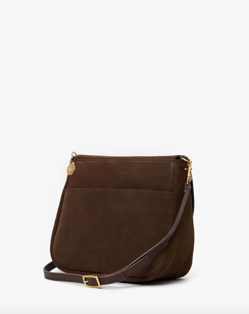 A dark brown suede crossbody bag with a flap closure and Bungalow-style gold-tone hardware, displayed against a plain white background by Turnlock Louis from Clare Vivier.