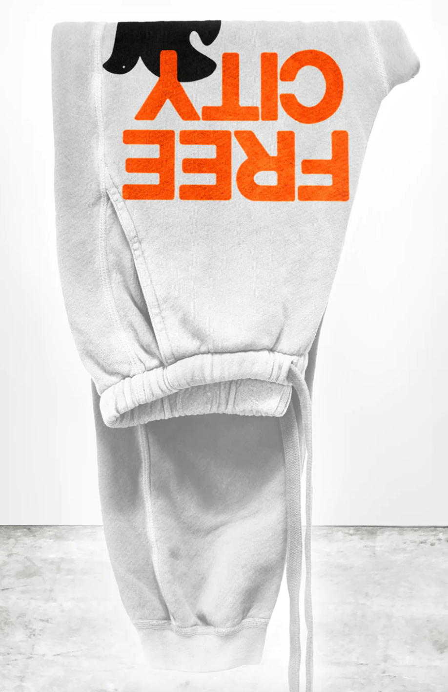 A white sweat pant with text in bold orange letters that reads "FREE CITY" displayed on a plain white background.
