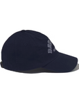 A navy blue, 100% cotton baseball cap featuring the word "DROP" and some smaller, indiscernible text embroidered on the side. The cap includes a curved brim and an adjustable closure at the back. Set against a plain white background, this stylish accessory radiates casual cool. This is the THE DROPOUT KAP NAVY by Kule.