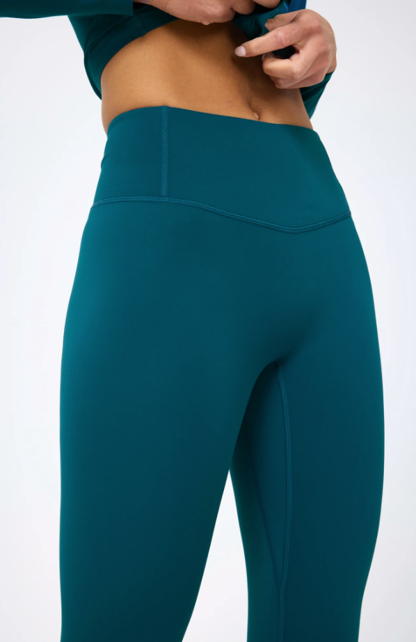 A close-up image of a woman wearing Terez's Action Basic Legging in Cypress, focusing on the fit and stitching details around the waist and hips. Only the lower torso and hands are visible, showcasing a style popular in Scottsdale, Arizona.