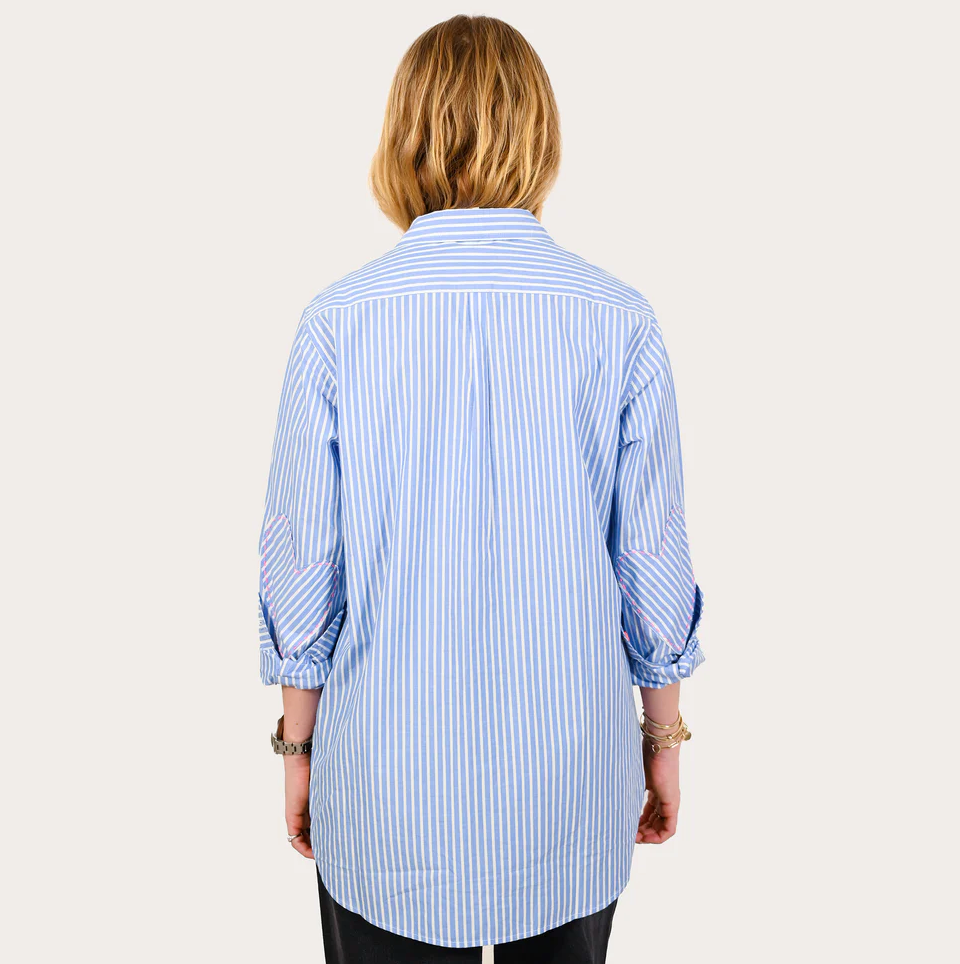 A woman stands with her back to the camera, wearing a Kerri Rosenthal Mia Shirt Stripe Blue/white Blue with rolled-up sleeves and black pants, isolated on a white background, capturing a casual Arizona style.