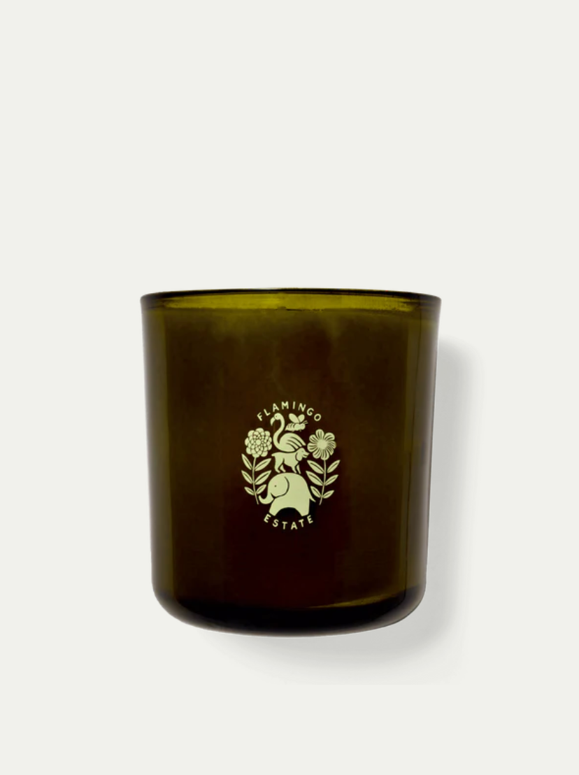 An Adriatic Muscatel Sage Candle with the logo &quot;Flamingo Estate&quot; featuring a palm frond and floral design, displayed against a plain white background in a Scottsdale Arizona bungalow.