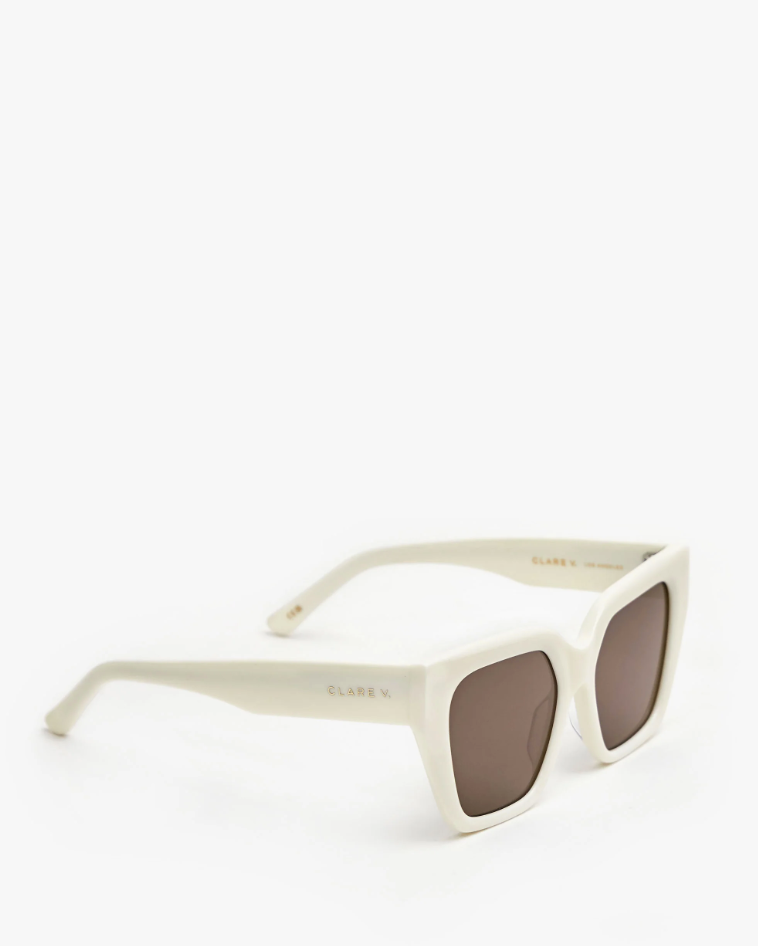 A pair of stylish Clare V. Heather Sunglasses Cream with thick frames and dark lenses, displayed against a white background. The brand name "Clare Vivier" is subtly inscribed on the arms, evoking the style of a luxurious Arizona bungalow.