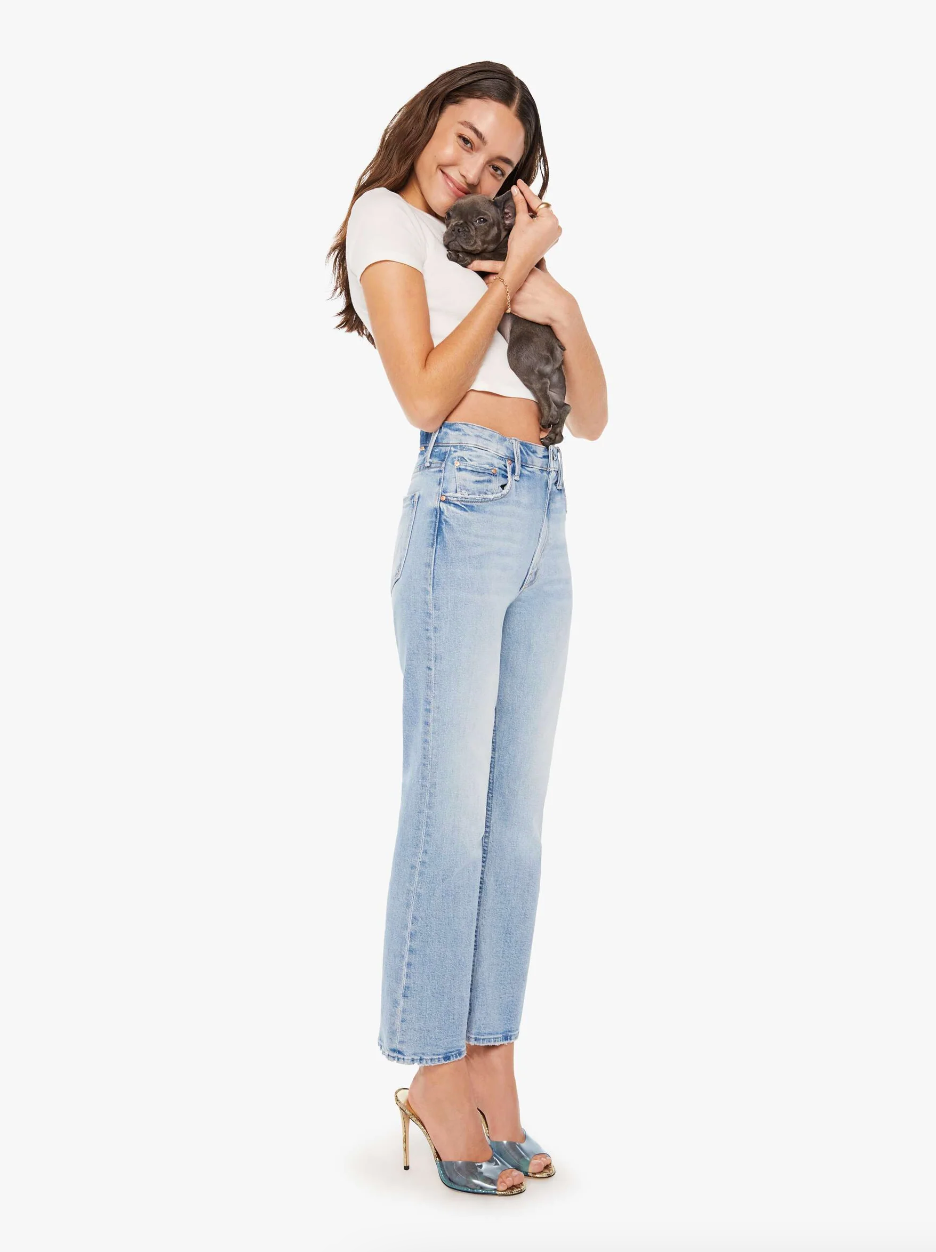 A woman stands smiling, wearing a white cropped top and light blue high-waisted jeans in her cozy bungalow. She is holding a small gray kitten close to her face. The woman is wearing high-heeled sandals and has long brown hair. Both look content and happy in Scottsdale, Arizona. The background is plain white.

(Note: As per your instructions, I did not mention a specific brand name.)