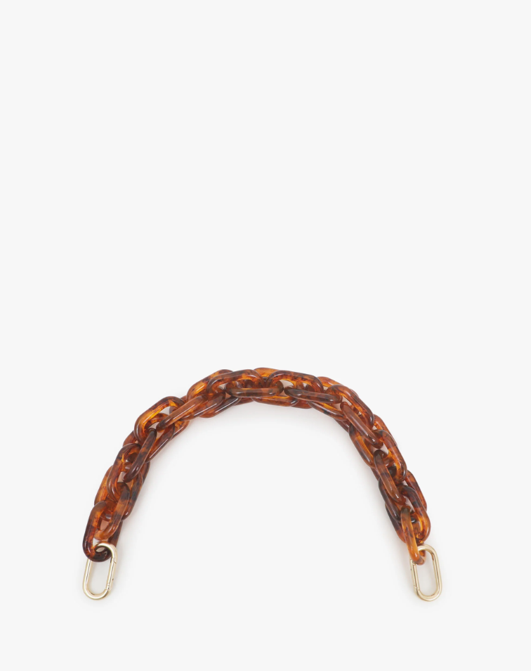 A close-up image of a Clare Vivier Shortie Strap with a tortoiseshell pattern. The strap features interlocking oval links in shades of brown and amber, with gold-colored rectangular clasps at each end. Brass spring links ensure it easily attaches to any bag. The strap is arranged in a semi-circular shape against a plain white background.