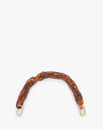 A close-up image of a Clare Vivier Shortie Strap with a tortoiseshell pattern. The strap features interlocking oval links in shades of brown and amber, with gold-colored rectangular clasps at each end. Brass spring links ensure it easily attaches to any bag. The strap is arranged in a semi-circular shape against a plain white background.