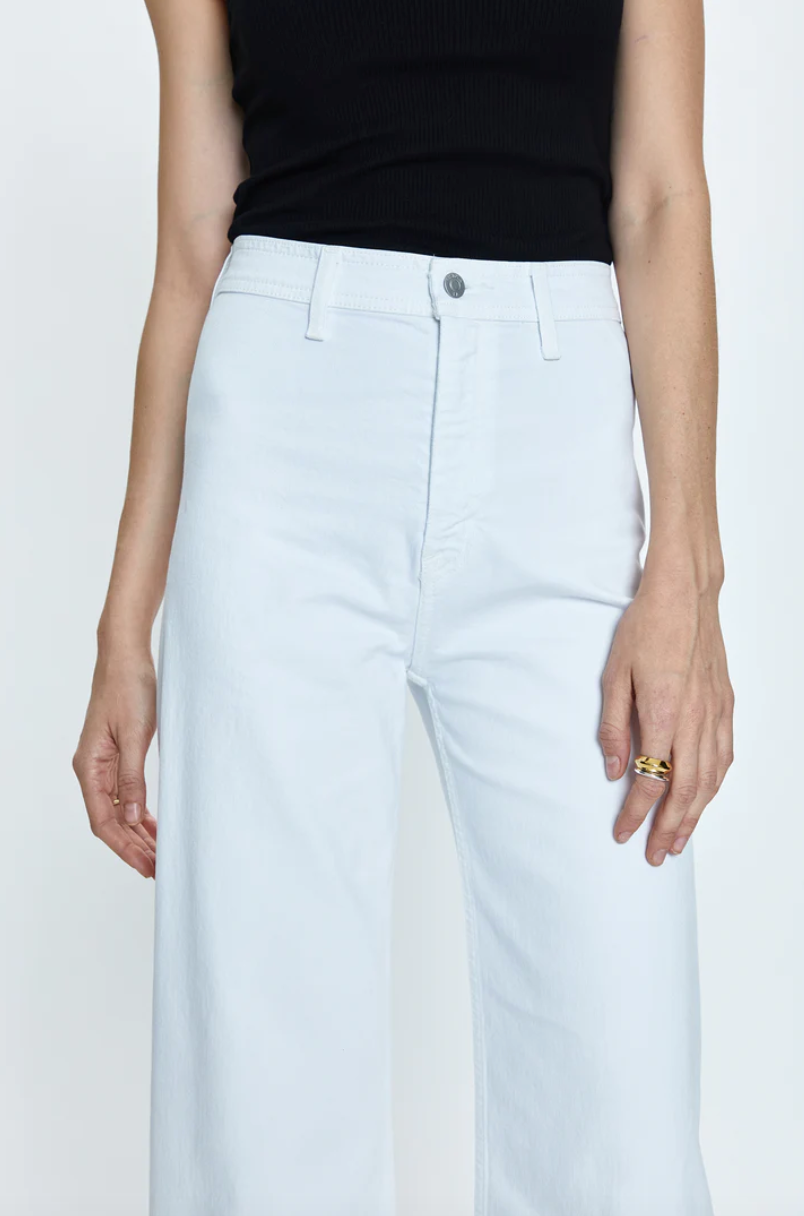 A close-up of a person wearing white jeans and a Pistola PENNY HIGH RISE WIDE LEG CROP - BLIZZARD top, Los Angeles-based black top, focusing on the waist and pocket detail with the person&#39;s hands by their sides.