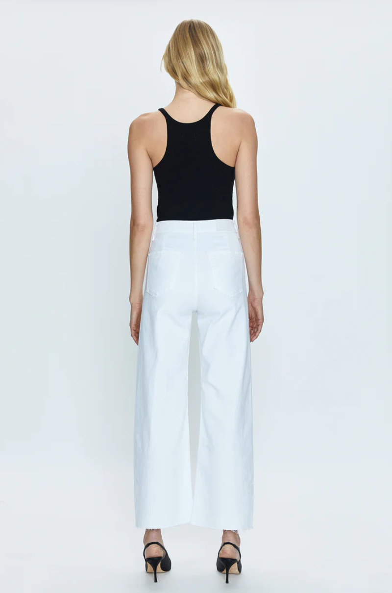 A woman standing with her back to the camera, wearing a Pistola black tank top and white Penny High Rise Wide Leg Crop - Blizzard pants, on a plain white background.