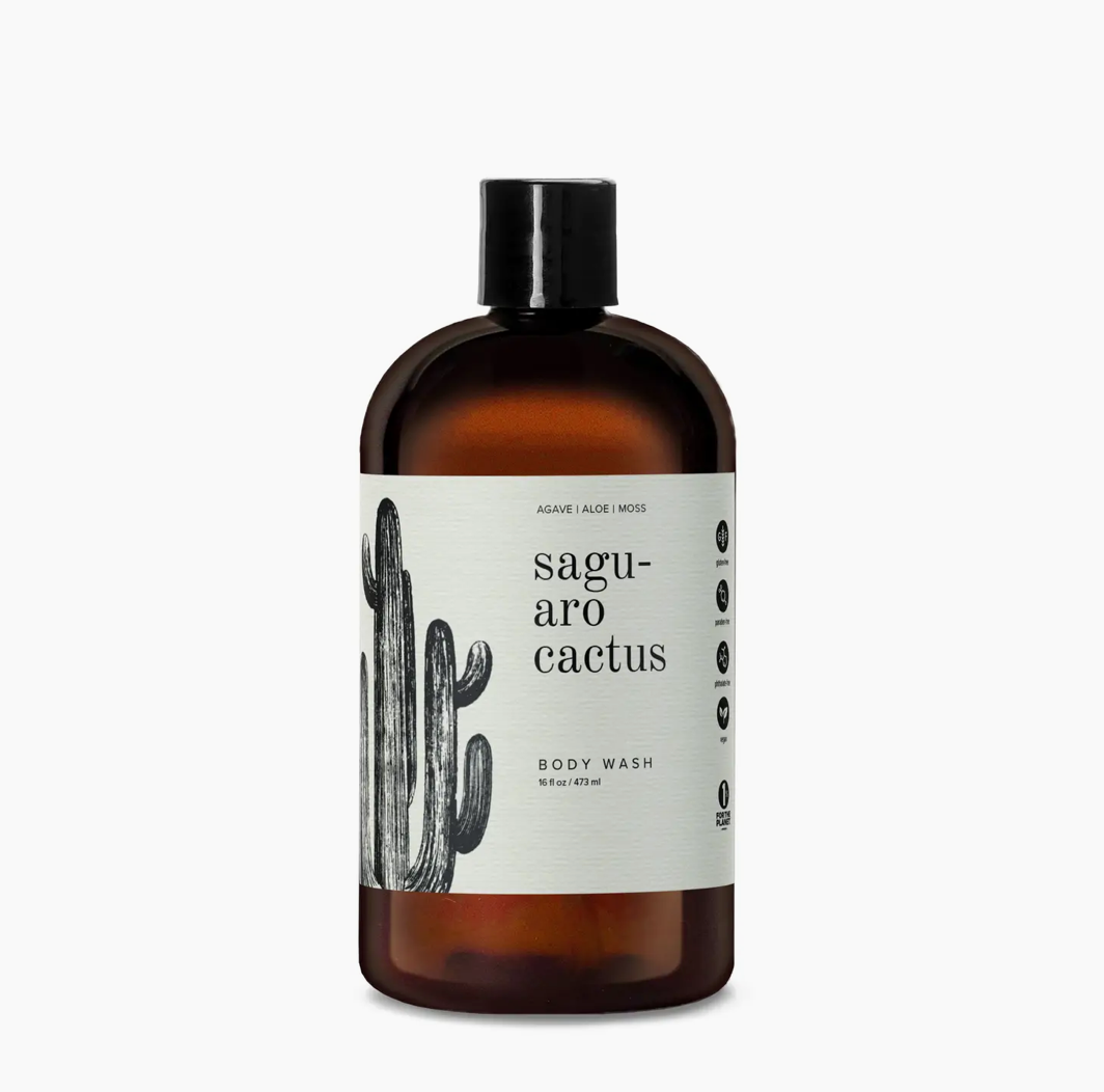 A bottle of Faire's "saguaro cactus" body wash with a minimalist label featuring a black sketch of a saguaro cactus on a cream background, set against a large amber glass bottle, inspired by the bungalow aesthetic of Scottsdale, Arizona.