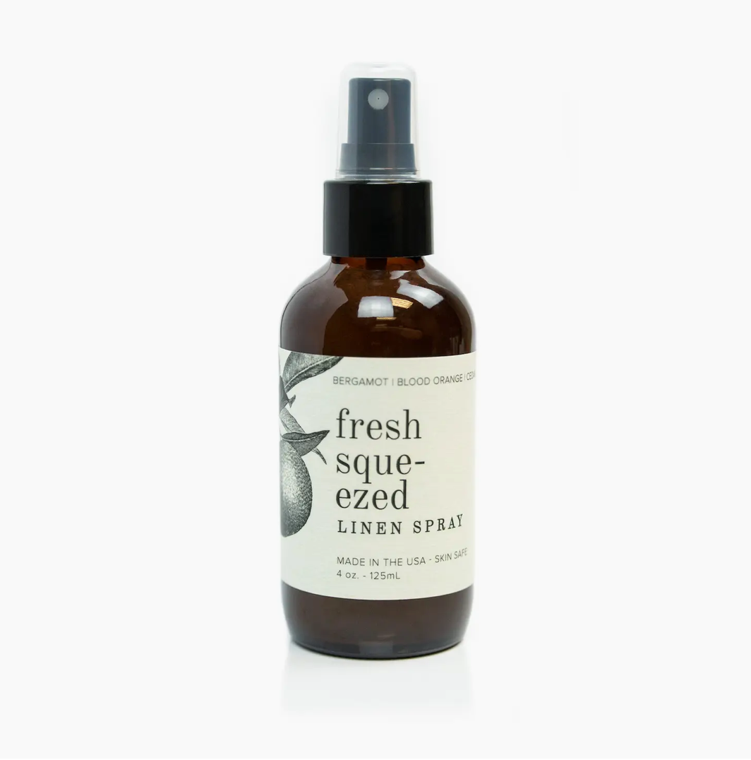A brown spray bottle labeled &quot;Faire Fresh Squeezed scent linen spray&quot; featuring bergamot oil and blood orange, on a white background.