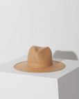 A light beige straw fedora hat with a wide brim, styled in a Arizona-inspired fashion, placed on a white surface against a white background, showcasing its texture and shape in soft lighting.