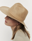 Profile view of a person with fair skin wearing a wide-brimmed Janessa Leone Simone Hat Sand in Arizona style, set against a plain white background.