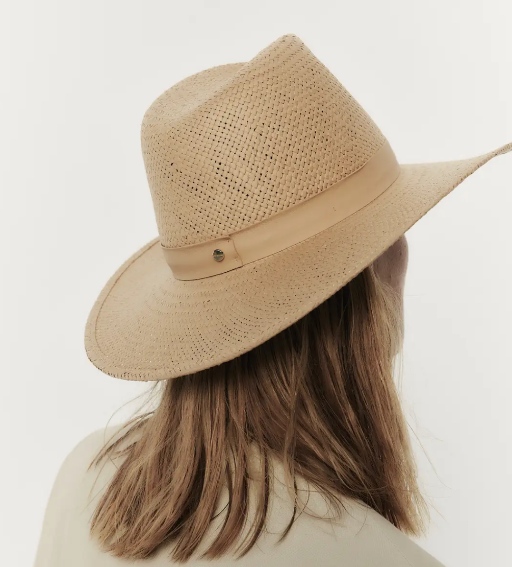Back view of a person with brown hair wearing a Janessa Leone SIMONE HAT SAND with a leather band, set against a white background. The person is also wearing a light beige top.