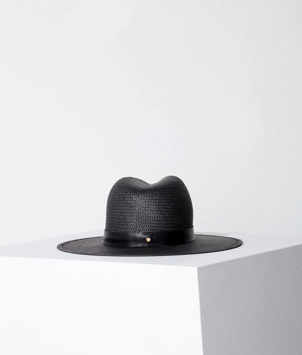 A SIMONE HAT BLACK by Janessa Leone placed on a white cylindrical pedestal against a light gray background, exuding Arizona style.