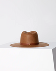 A Janessa Leone SHERMAN HAT BROWN rests on a white cube against a two-tone gray and white background, emphasizing its distinct Arizona style and texture.