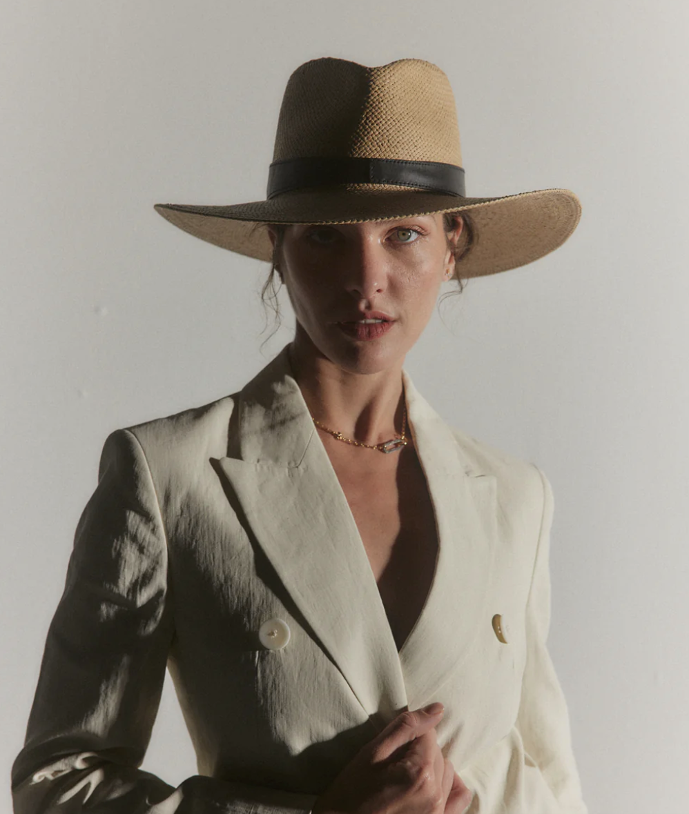 A woman with a piercing gaze wearing a beige blazer and a Janessa Leone Savannah Hat Sand, captured against an Arizona desert background, highlighting subtle shadows on her face.