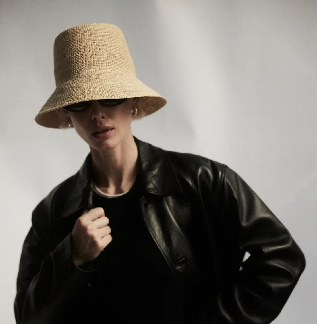A stylish woman in a black leather jacket and a FELIX BUCKET NATURAL hat covering her eyes poses against a light gray background, evoking the casual Arizona vibe. Brand Name: Janessa Leone