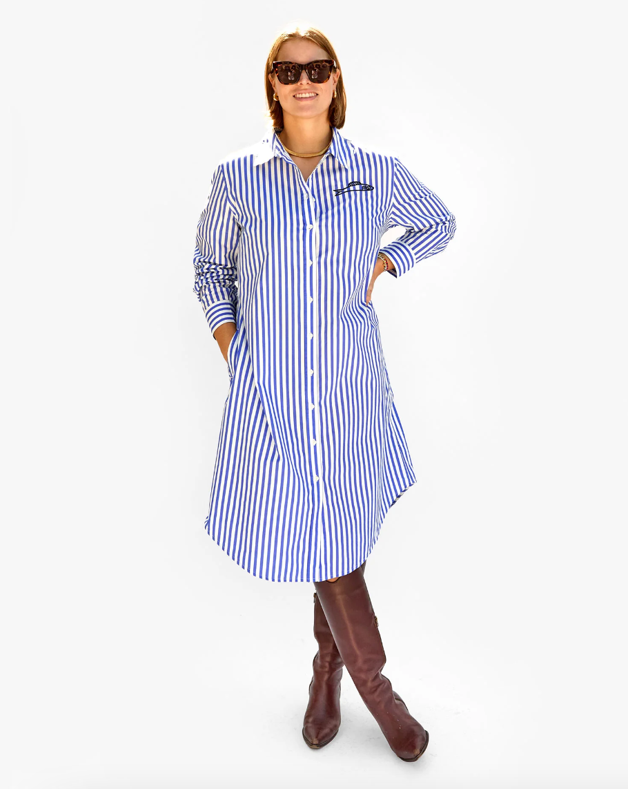 A woman in sunglasses and Arizona-style knee-high boots stands confidently with her hands on her hips, wearing a Clare Vivier Suzette Dress Blue & Cream Stripe w/ Sardine against a white background.