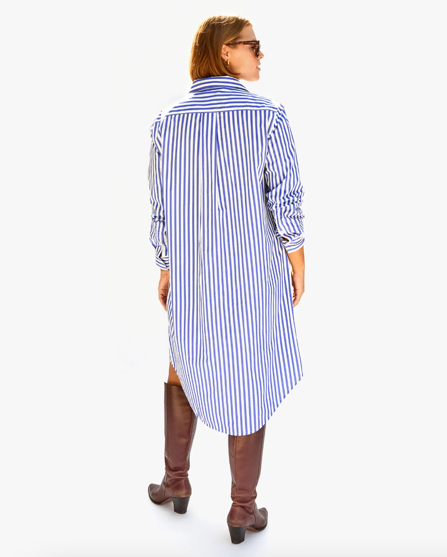 A woman viewed from the back, wearing a Suzette Dress Blue &amp; Cream Stripe w/ Sardine from Clare Vivier paired with tall brown boots. She has sunglasses on and her hair is styled in a bun, embodying Arizona style.