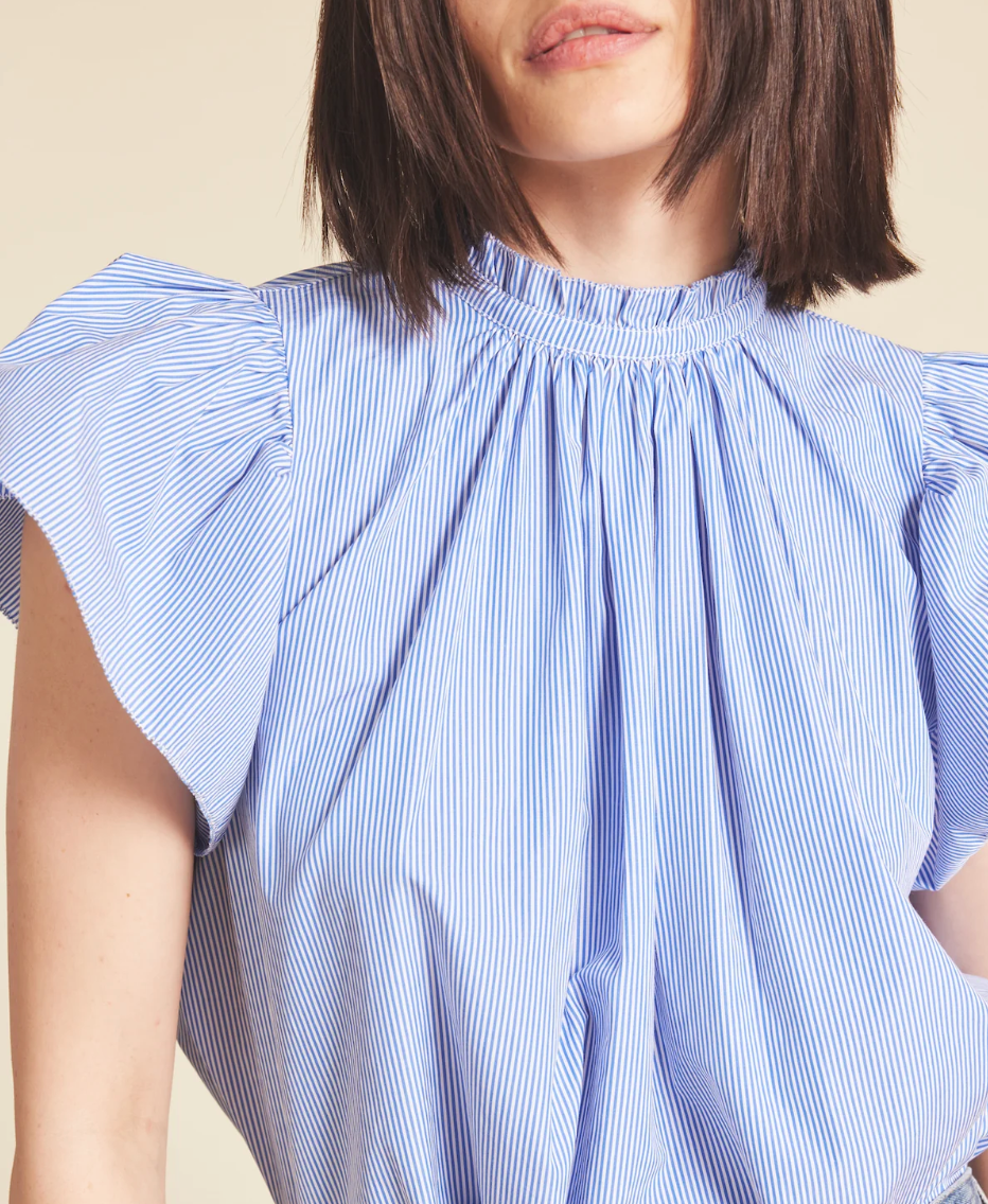 A close-up of a woman wearing a Trovata CARLA HIGHNECK SHIRT BLUE/WHITE STRIPES with unique gathered shoulders and a high neckline, photographed in Scottsdale, Arizona. Only her torso and chin are visible.