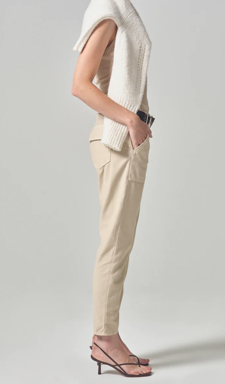 A person wearing the Leah Cargo In Taos Sand sateen pants from Citizens Of Humanity stands with one hand in a pocket outside a Scottsdale, Arizona bungalow, showcasing a chic, casual outfit. The focus is on the clothing and simple elegance.