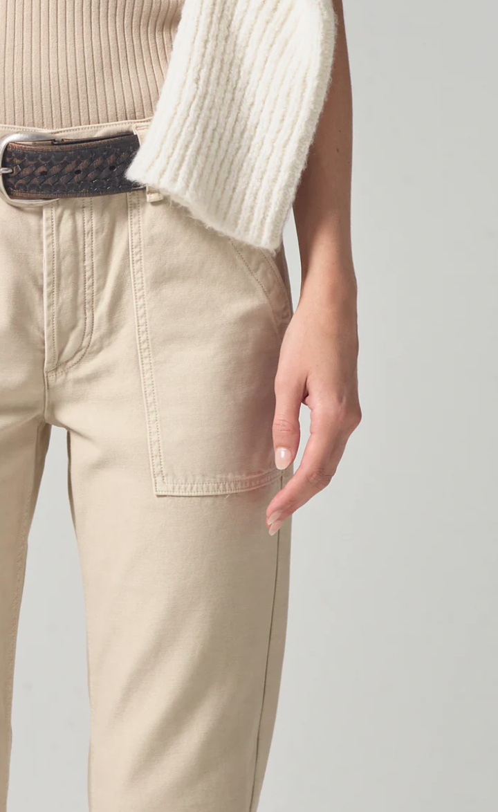 Close-up of a person wearing the Leah Cargo In Taos Sand (sateen) trousers by Citizens Of Humanity/AGOLDE and a beige sweater with a white cardigan draped over one shoulder, focusing on the pocket detail and hand placement in Scottsdale, Arizona.