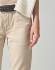 Close-up of a person wearing the Leah Cargo In Taos Sand (sateen) trousers by Citizens Of Humanity/AGOLDE and a beige sweater with a white cardigan draped over one shoulder, focusing on the pocket detail and hand placement in Scottsdale, Arizona.