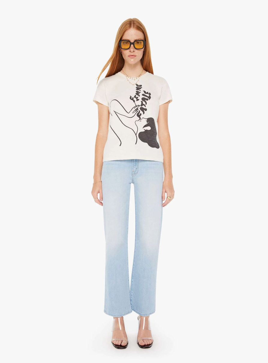 A woman stands facing the camera, wearing a white T-shirt with a black abstract design, light blue jeans, sunglasses, and heeled sandals by Mother's The Sinful Femme Fatale in Scottsdale Arizona.