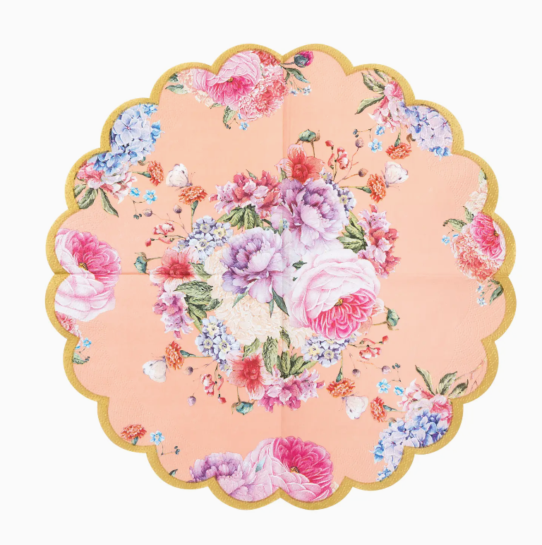 A scalloped, circular fabric placemat featuring a vibrant floral print with various colors including pink, blue, and white flowers on a pastel peach background, perfect for a Faire bungalow.