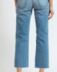A person from behind wearing ASKK's berkeley low rise straight cropped blue jeans with frayed hems in Arizona style, standing barefoot on a white background.