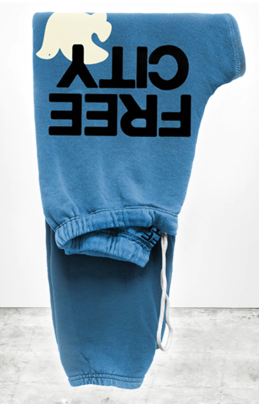 Blue unisex FREECITY large sweatpants with the words "FREE CITY" printed in bold black font. The pants have a drawstring and are hung vertically against a white backdrop.
