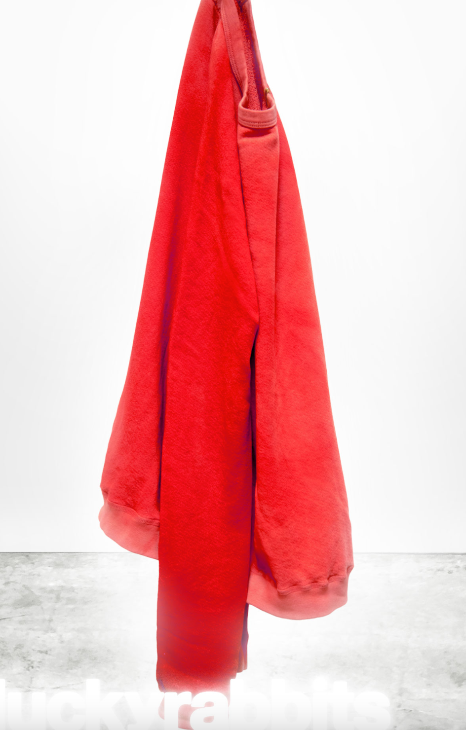 A vibrant red towel hanging on a hook against a white background with a shadow on the floor, displaying the text "Lucky Rabbits Sweatshirt" at the bottom in a bungalow by Free City (sparrow, LLC).