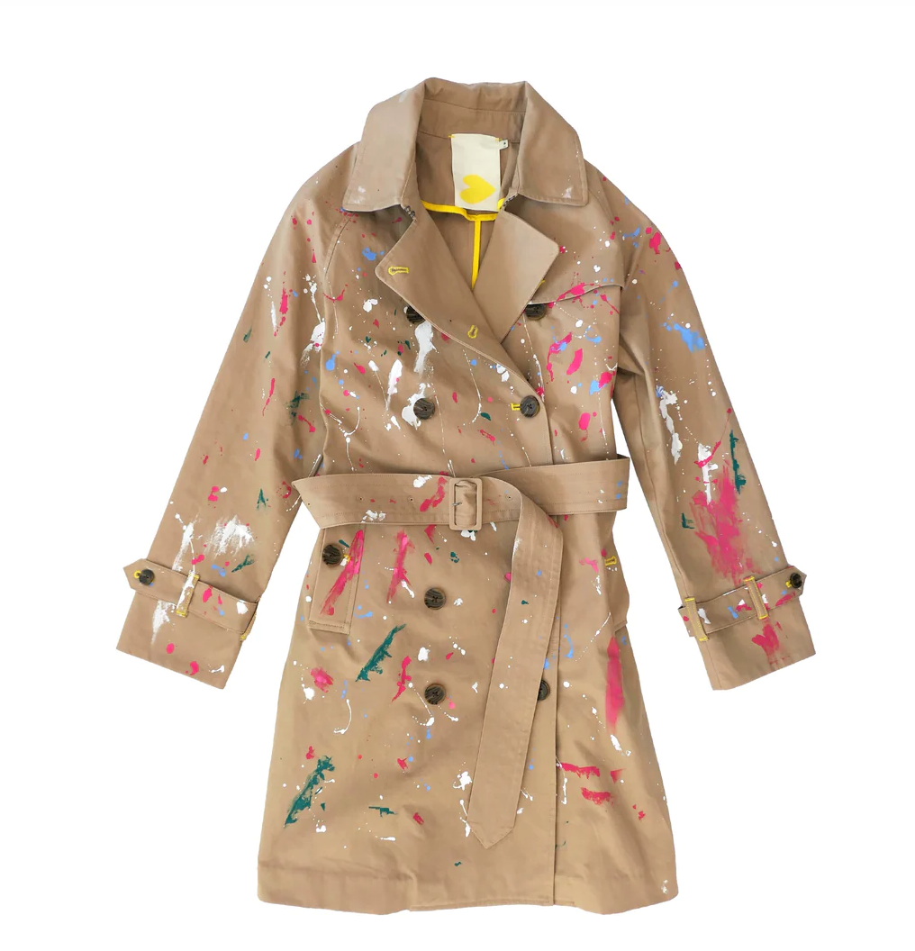 A beige KR Trench with multicolored paint splatters displayed against the backdrop of a Scottsdale, Arizona bungalow, featuring a belt and large collar.