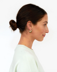 Clare Vivier Le Hoop earrings in gold, worn by a woman in a white sweater with hair in a low bun, profile view.