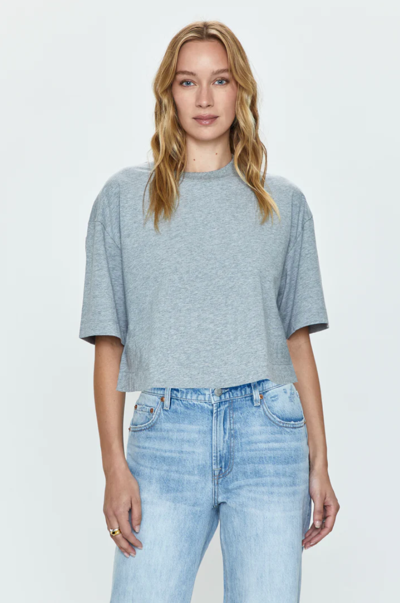 A Los Angeles-based woman with long blonde hair wearing a Pistola Mae Cropped Tee and blue faded jeans stands against a white background.