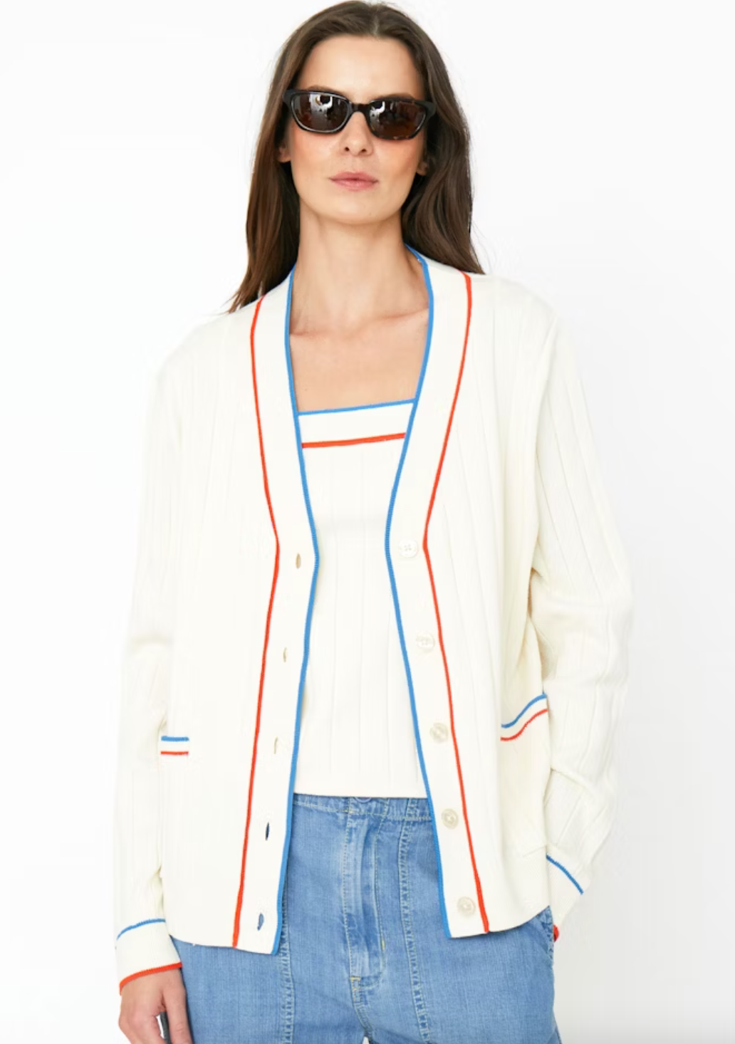 A woman wearing sunglasses models a white button-up cardigan with blue and red trim, styled over a matching striped shirt and blue jeans in Scottsdale, Arizona.