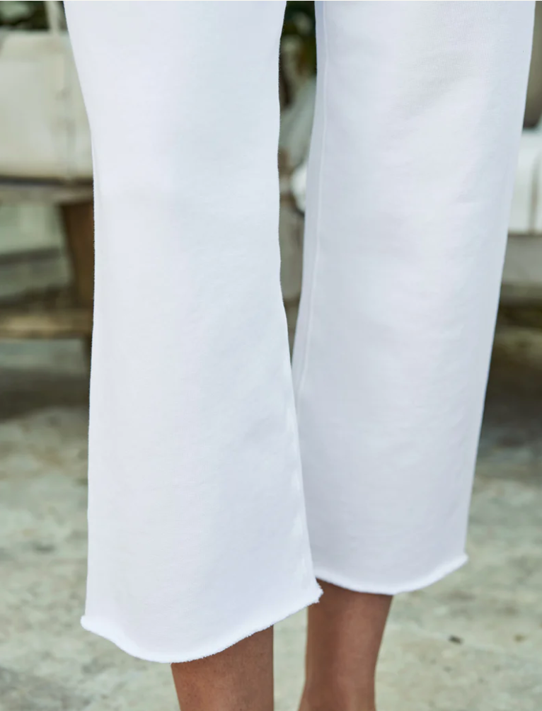 Close-up of a person&#39;s lower legs wearing white Frank &amp; Eileen CATHERINE Favorite Sweatpant TRIPLE FLEECE trousers. The background shows a blurred natural setting near a bungalow in Scottsdale, Arizona, emphasizing the elegant simplicity of the outfit.