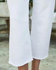 Close-up of a person's lower legs wearing white Frank & Eileen CATHERINE Favorite Sweatpant TRIPLE FLEECE trousers. The background shows a blurred natural setting near a bungalow in Scottsdale, Arizona, emphasizing the elegant simplicity of the outfit.