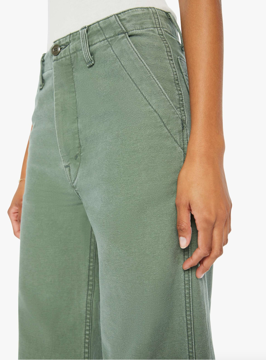 Close-up of a person wearing Mother green jeans in Scottsdale, Arizona, focusing on the pocket detail with a hand lightly resting on the thigh.