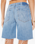 Rear view of a woman wearing The Down Low Undercover Short Fray Wash by Material Girl in Scottsdale, Arizona, showing the pocket details and seams. The shorts are knee-length with a faded blue wash.