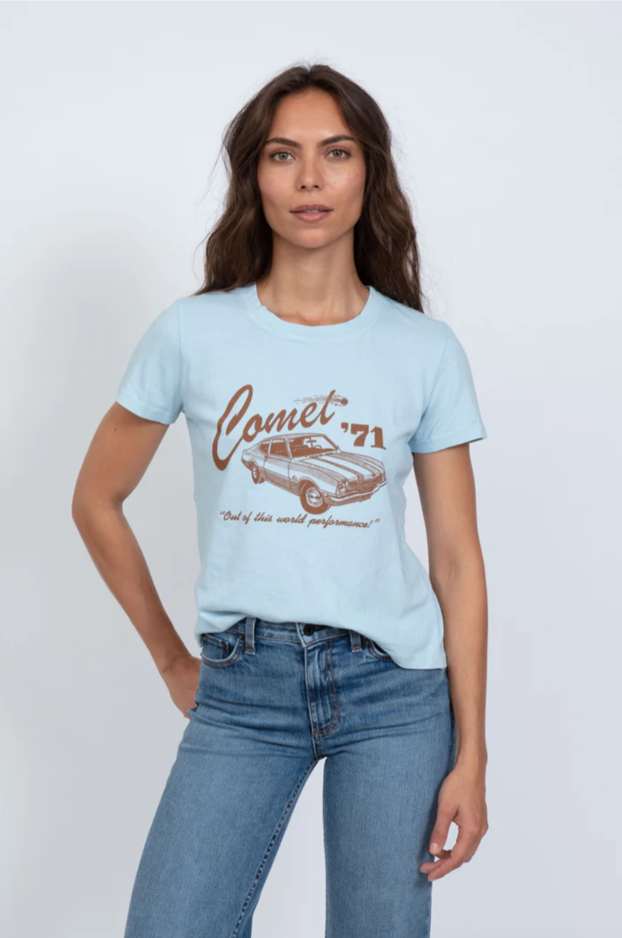 A woman with long brown hair wearing a ASKK printed classic tee with "Comet '71" and an illustration of a car, paired with light blue jeans, standing against a white background in Scottsdale, Arizona.