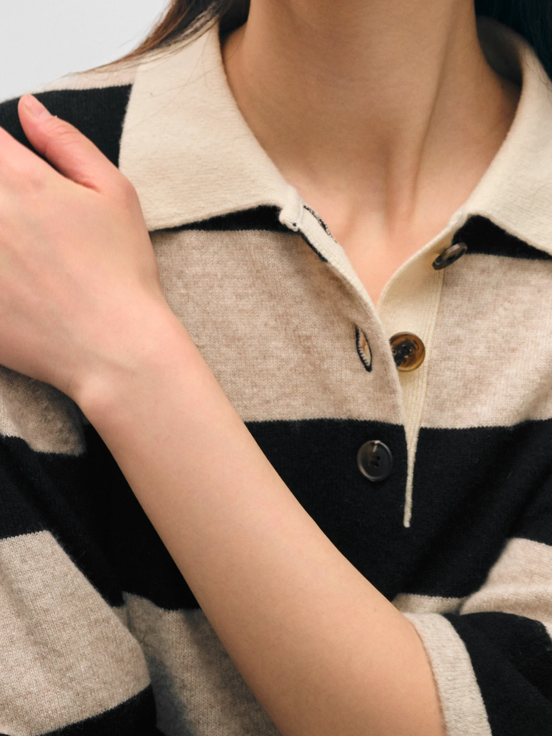 Close-up of a woman wearing a White + Warren Cashmere Crop Striped Polo Sandwisp/black jacket with large buttons, focusing on the collar and upper chest area. Her hand is resting on her shoulder in Scottsdale, Arizona.
