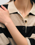 Close-up of a woman wearing a White + Warren Cashmere Crop Striped Polo Sandwisp/black jacket with large buttons, focusing on the collar and upper chest area. Her hand is resting on her shoulder in Scottsdale, Arizona.
