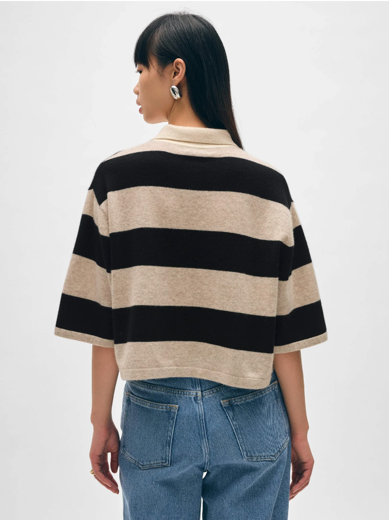 A woman with her back to the camera, wearing a White + Warren Cashmere Crop Striped Polo in Sandwisp/black and blue jeans, is standing outside a bungalow in Scottsdale, Arizona. She has straight, black hair and is wearing minimalist earrings.