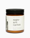 A Faire soy candle in a glass jar labeled "saguaro cactus" with "agave, aloe, moss" written beneath. The jar is brown with a black lid and the label includes an illustration of a cactus.