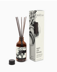 A Faire reed diffuser in an amber glass bottle labeled "apricot bloom" with several dark sticks inserted, positioned next to its floral-decorated packaging box, perfect for home decor.