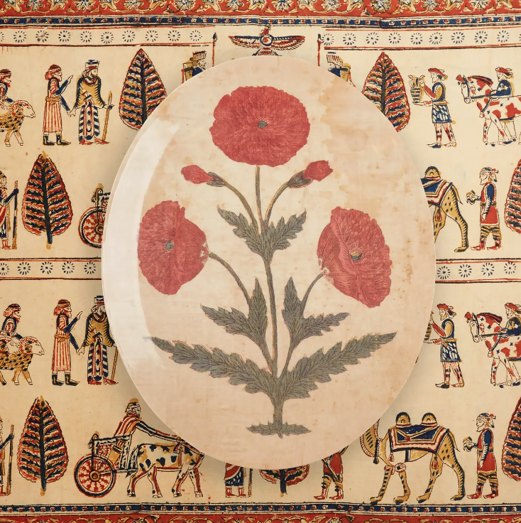An oval-shaped ceramic plate decorated with a design of three red poppies against a Faire-style tablecloth featuring ancient figures and hieroglyphics.